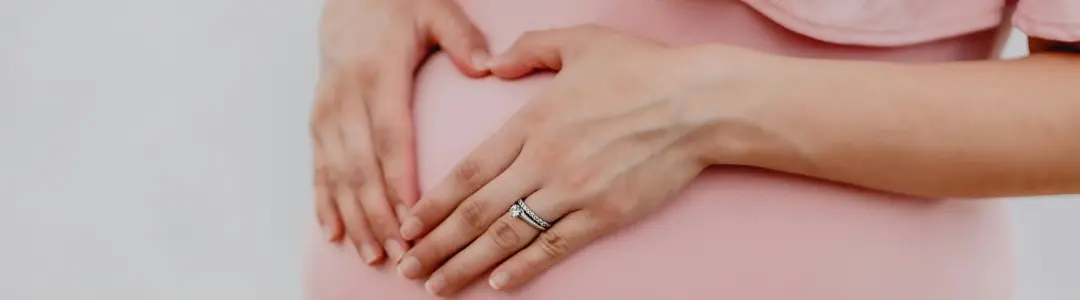 Carole Scheeck-Lorentz, sage-femme, femme enceinte avec une jolie robe rose qui tient ses mains en coeur sur son ventre, image foire aux questions